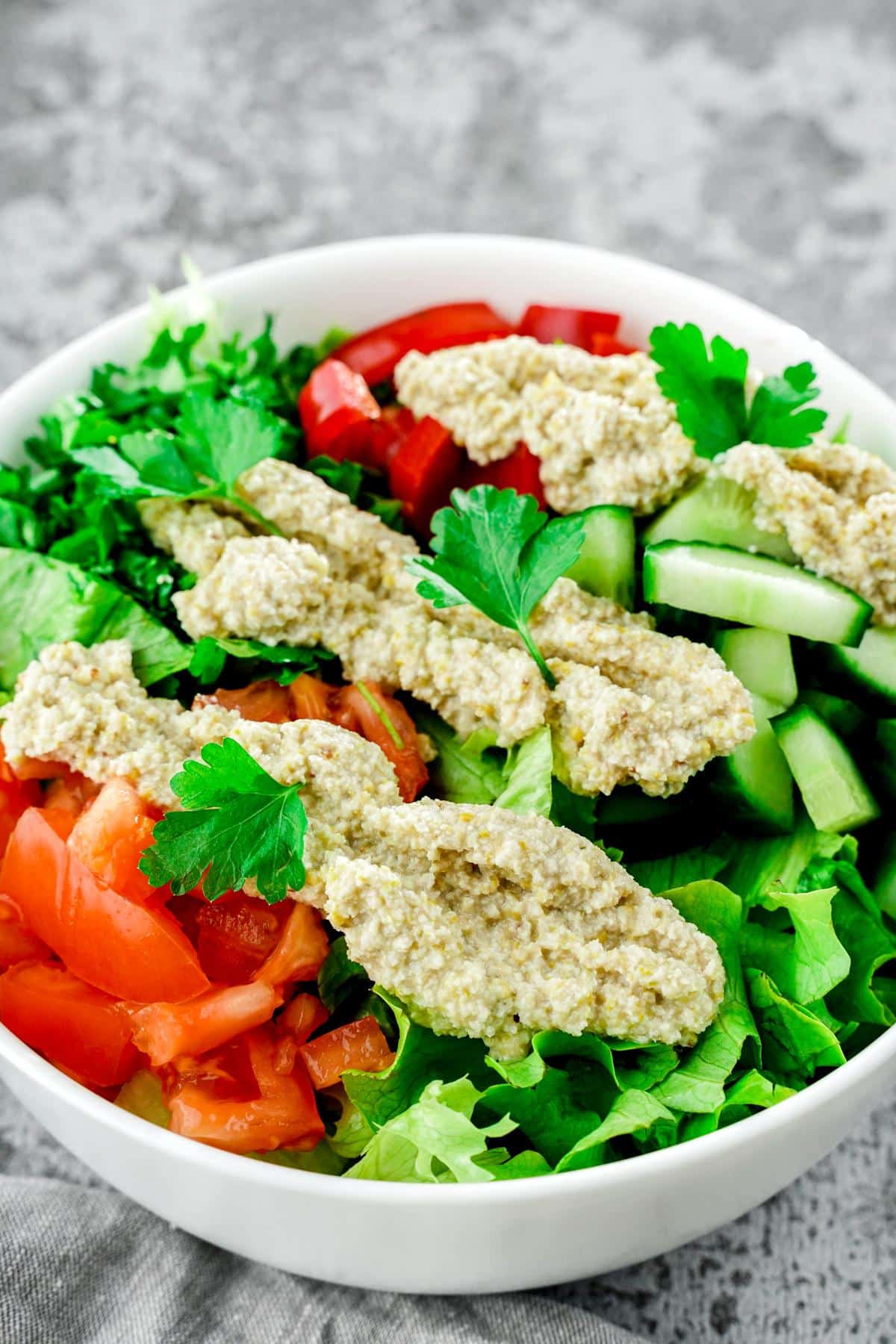 large white bowl of salad topped with dressing sitting on gray marble surface