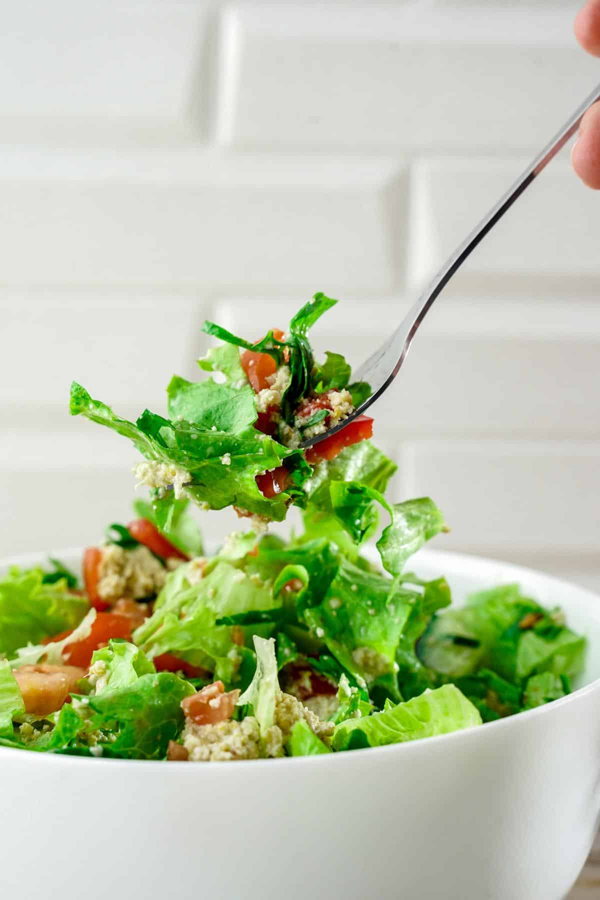 fork of salad above white bowl on table with tile background