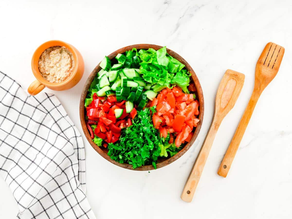 large wooden bowl of salad on white table by checked napkin and wooden spoons