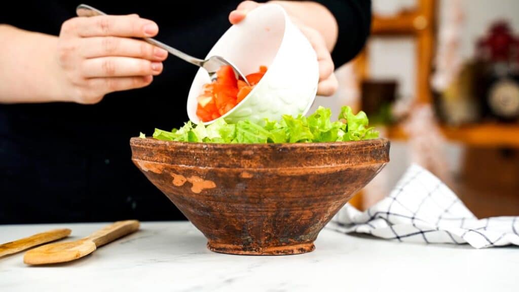 tomato being poured into bowl of salad