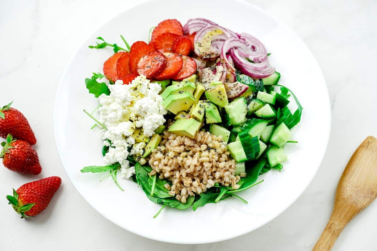 white bowl of salad with strawberries and red onions on top