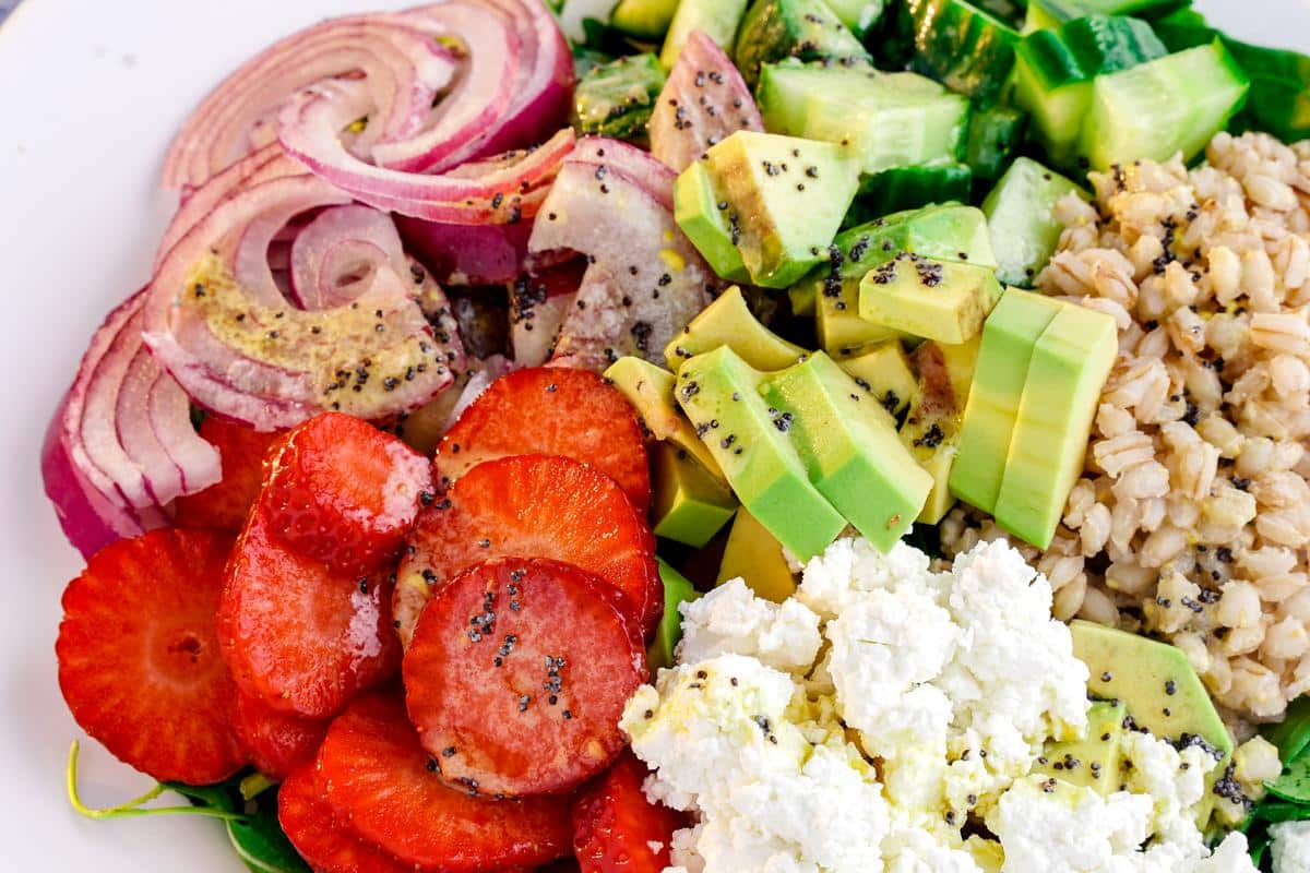 farro salad with bright red strawberries on top of white bowl