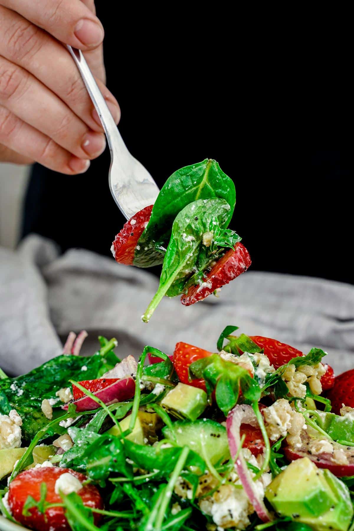 fork of salad held above bowl in front of blue tablecloth