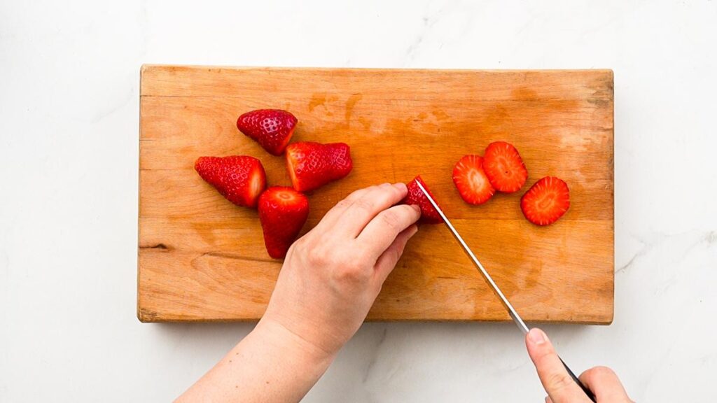 strawberries being sliced on cutting board