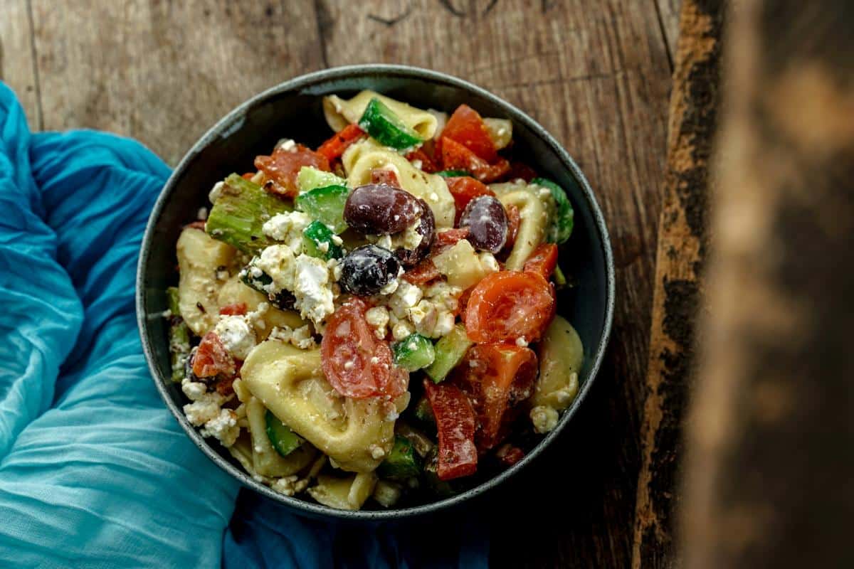 wooden bowl of tortellini pasta salad on wood table next to light blue napkin