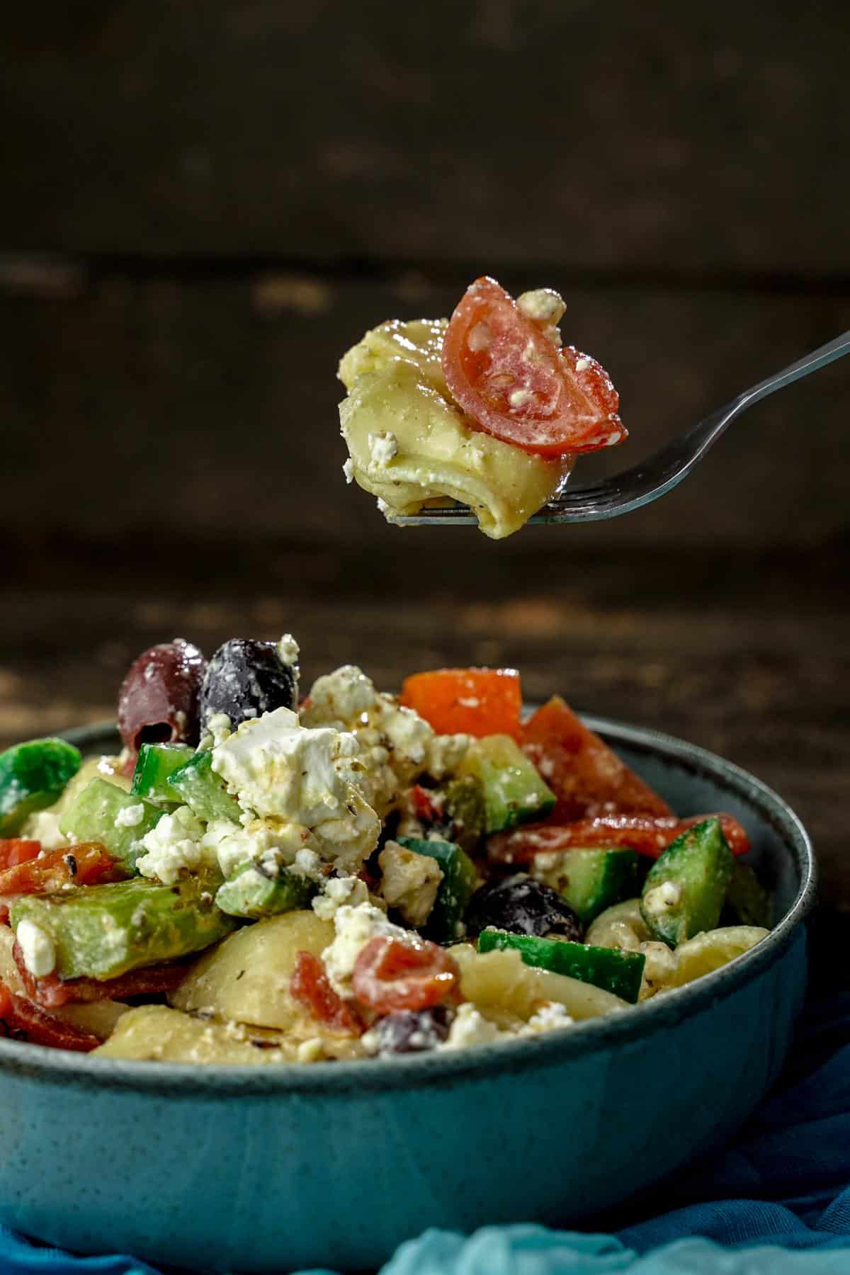 fork holding pasta above teal bowl of Greek tortellini pasta salad
