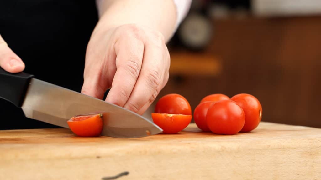 hand slicing tomatoes on cutting board