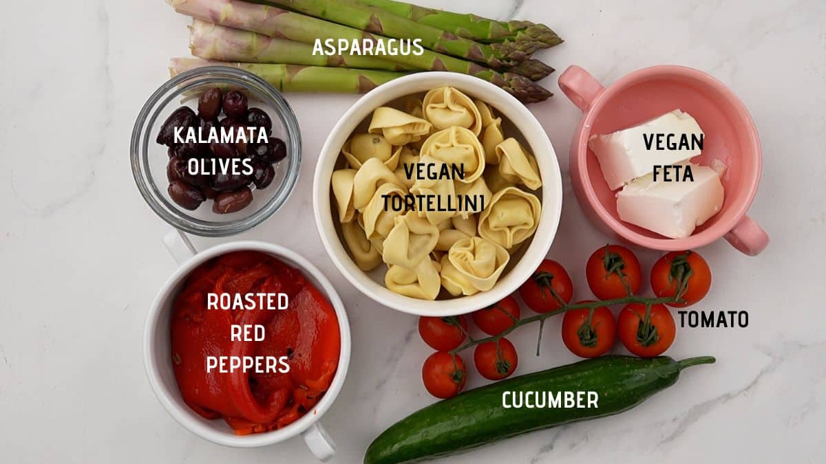 pasta in a bowl in the middle of a table of vegetables for making pasta salad