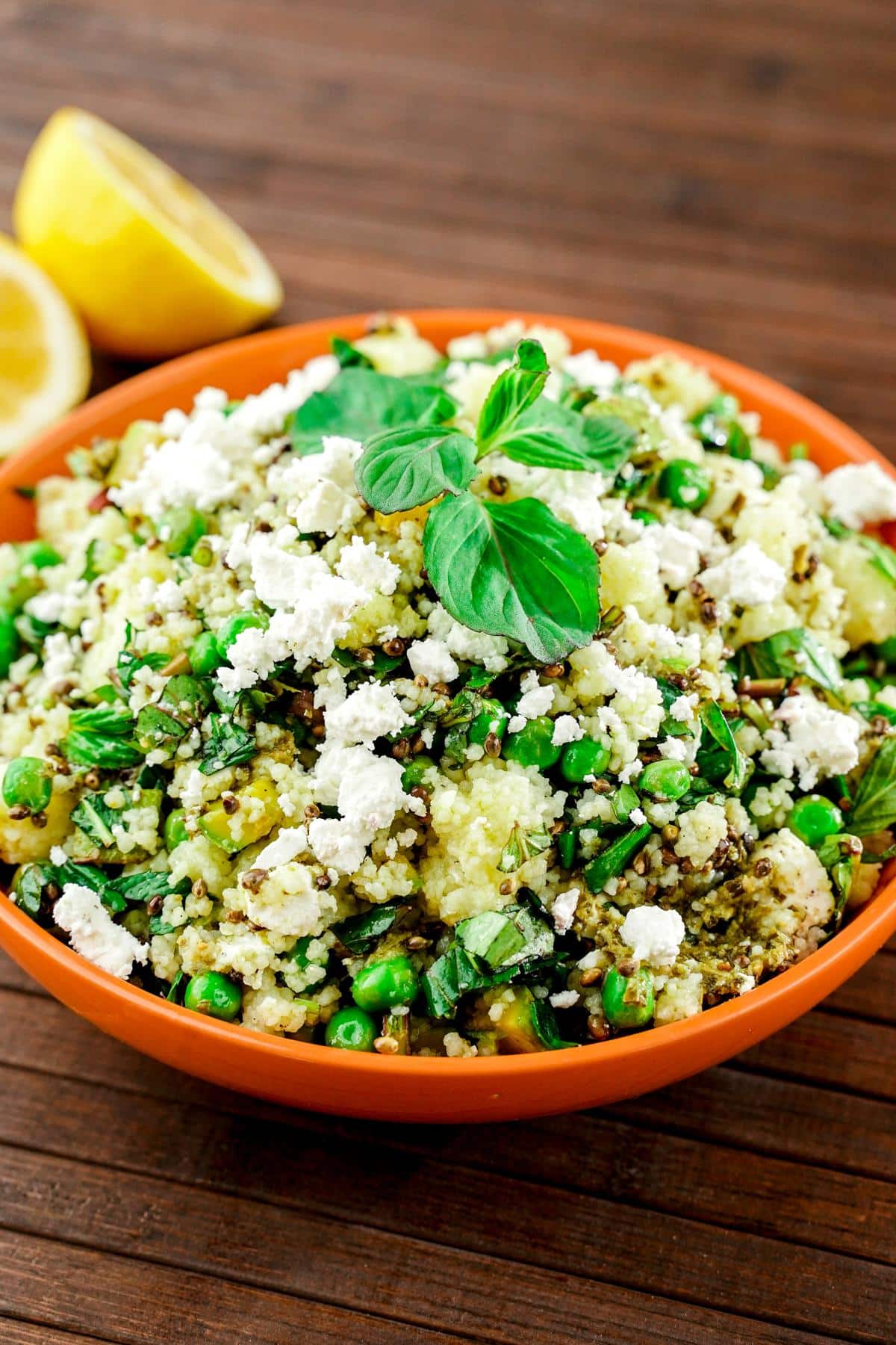 orange bowl of couscous salad on wood table by lemon halves