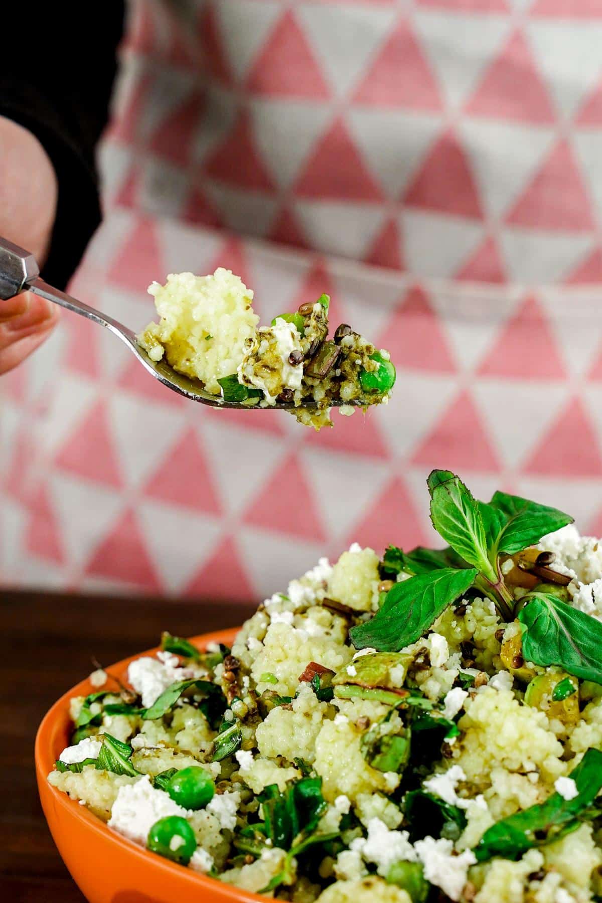 hand holding spoon of couscous salad above bowl