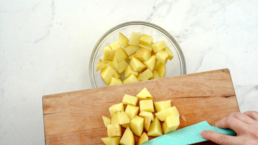 cubed potatoes being added to wood board