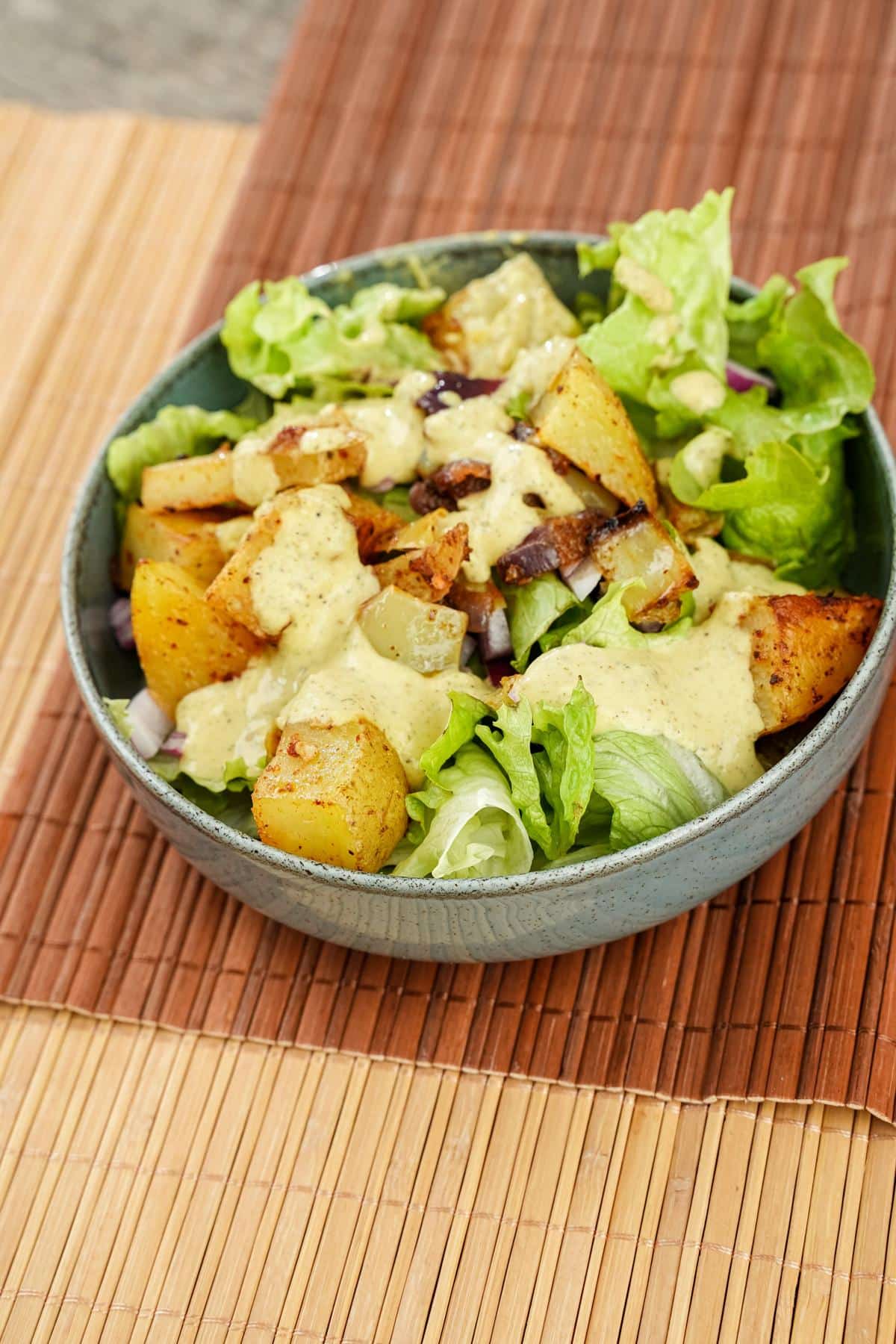 bowl of salad topped by roasted vegetables on bamboo placemat