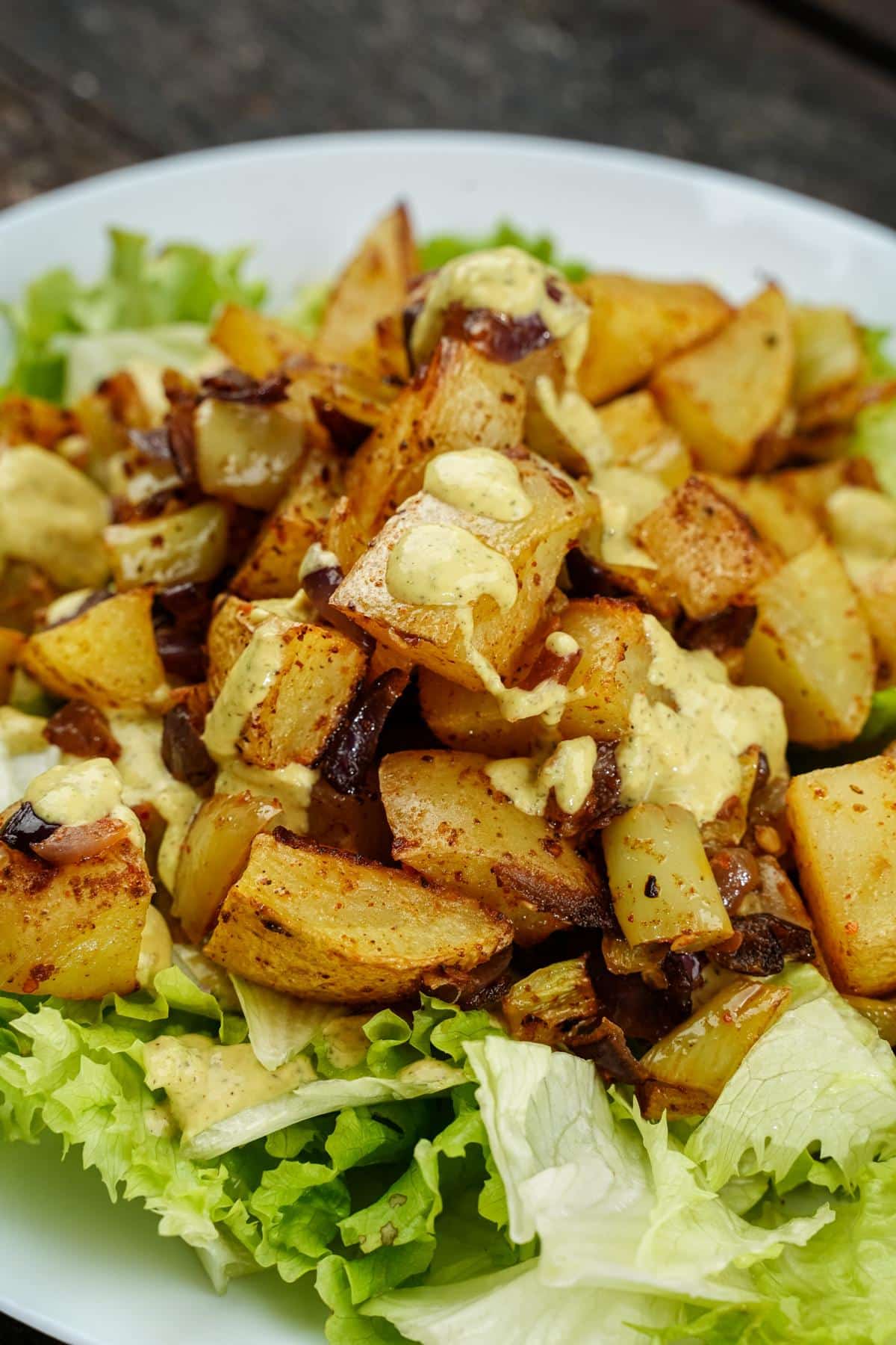 white bowl of spicy potatoes on bed of lettuce