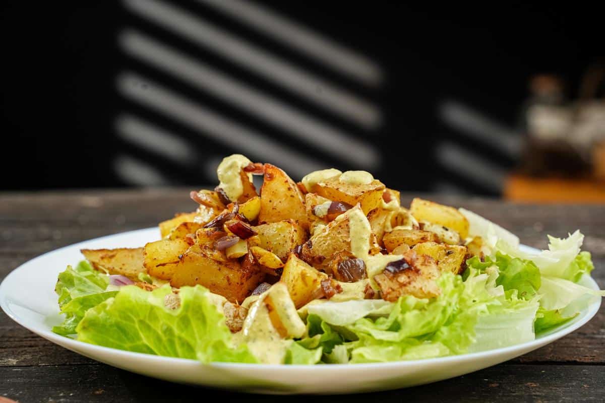 white plate of lettuce topped with spicy potato bowl and tahini dressing