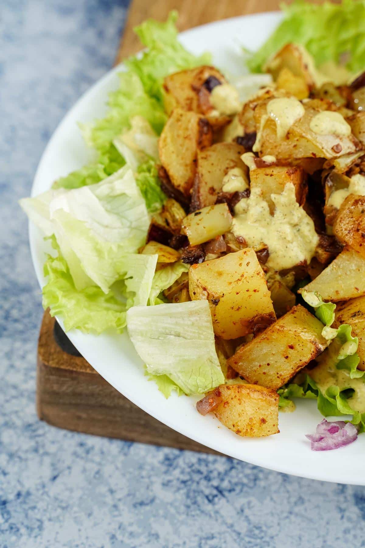 white plate of lettuce and spicy potatoes with dressing