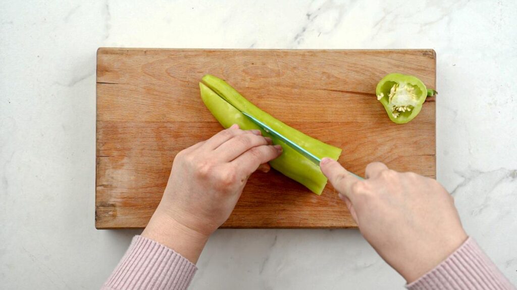 knife cutting green pepper on wood board