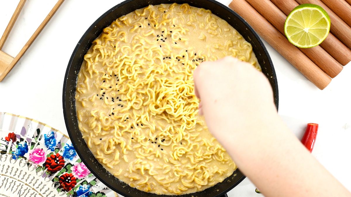 hand adding sesame seeds to wok of ramen 