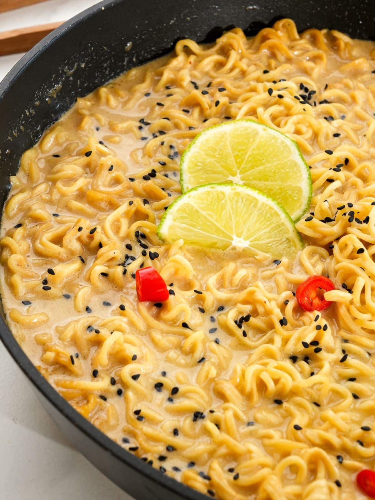 lime and chili slices on top of black wok of Thai peanut ramen