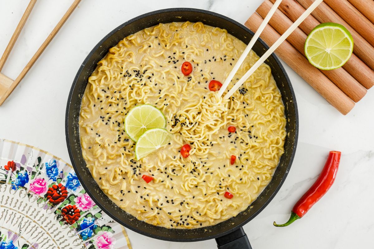 large black pan of ramen on white table with fresh chili and lime on the side