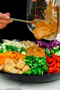 thai sauce being poured over salad in black bowl