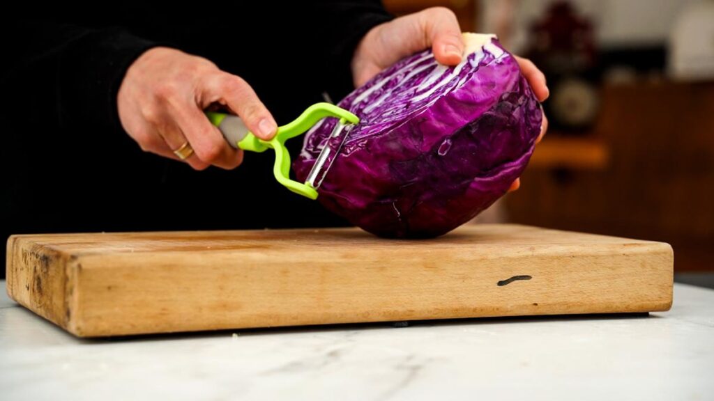 purple cabbage being shredded on top of cutting board