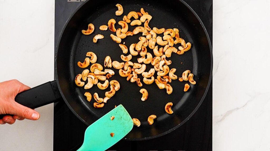 cashews in skillet with teal spatula