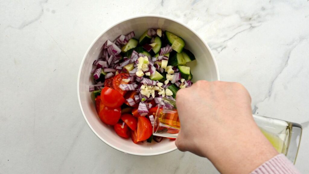 adding oil to white bowl of salad