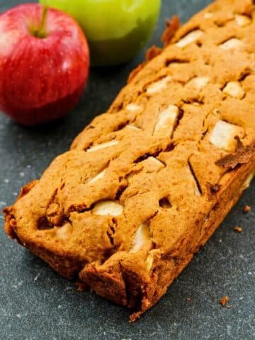 loaf of apple spice bread on black table by fresh apples