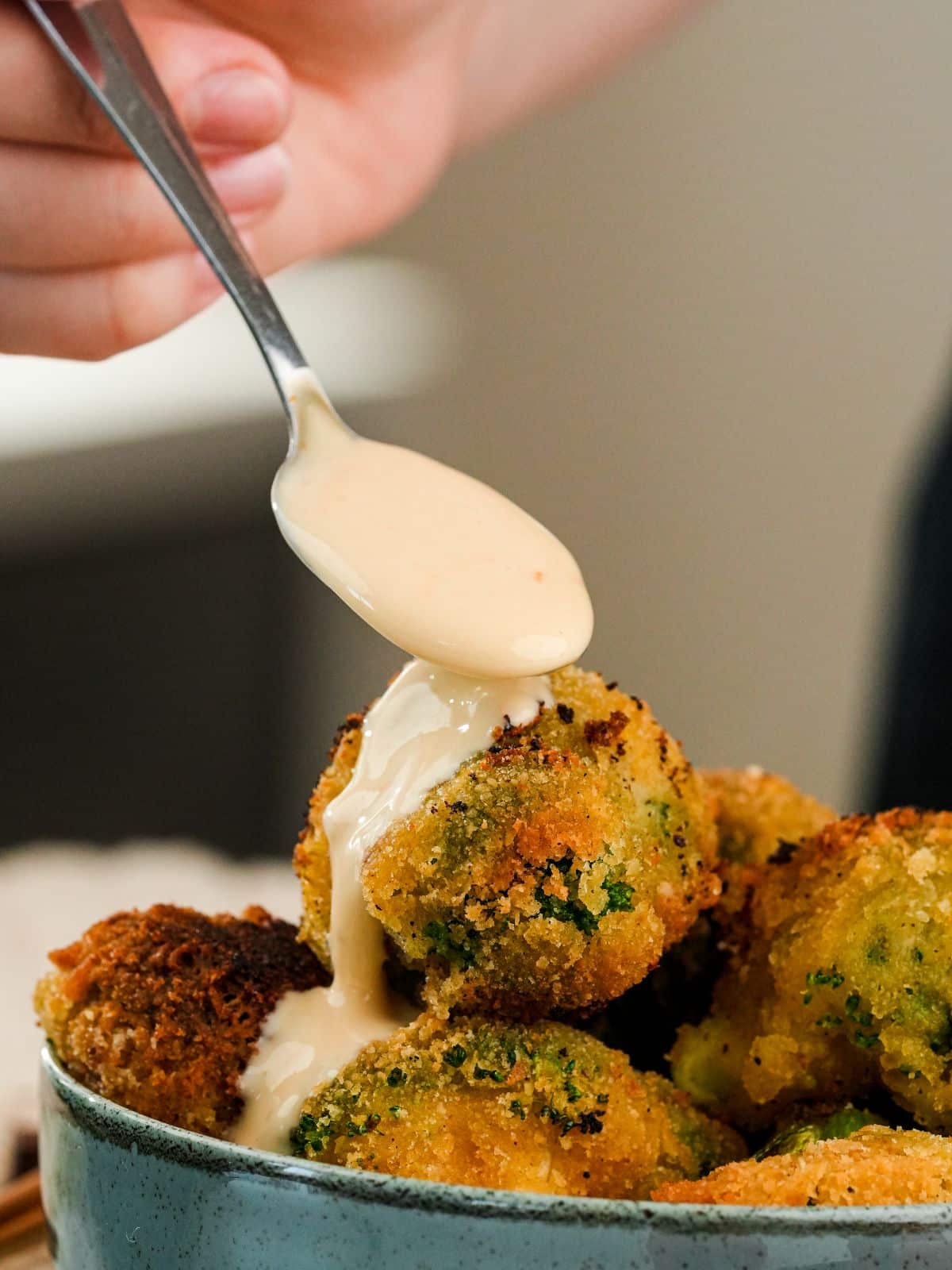 spoon of bang bang sauce being poured over fried bang bang broccoli in large blue bowl