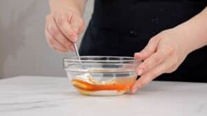 hand stirring orange sauce in glass bowl on marble counter