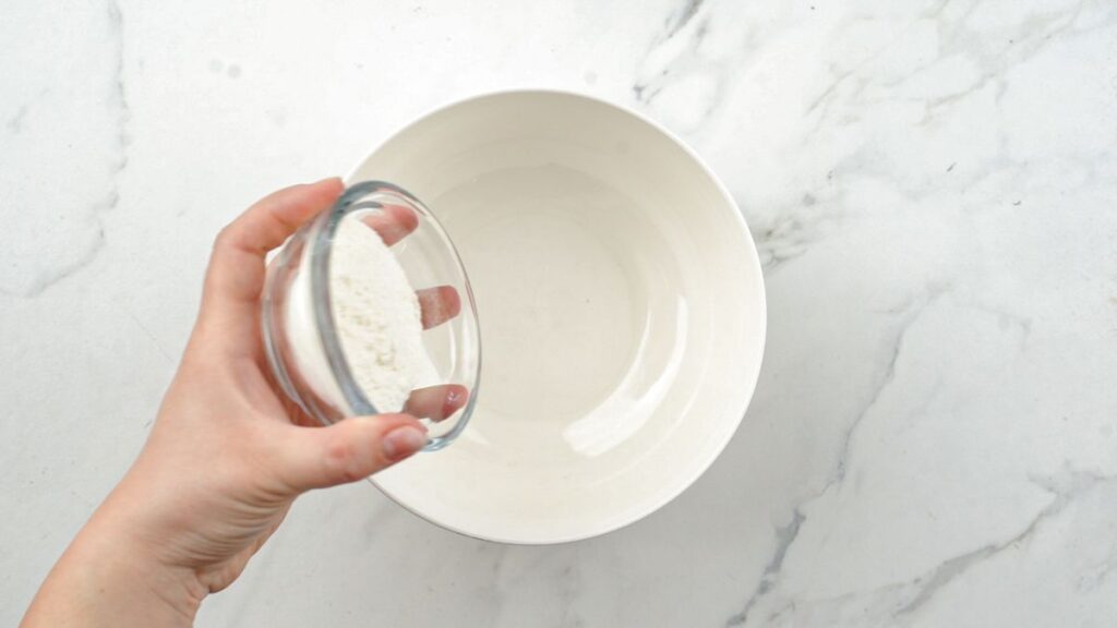 glass bowl of water held above white bowl on marble table