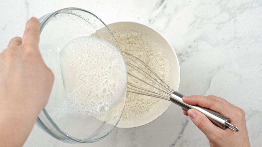 liquid in glass bowl being poured into white bowl of flour