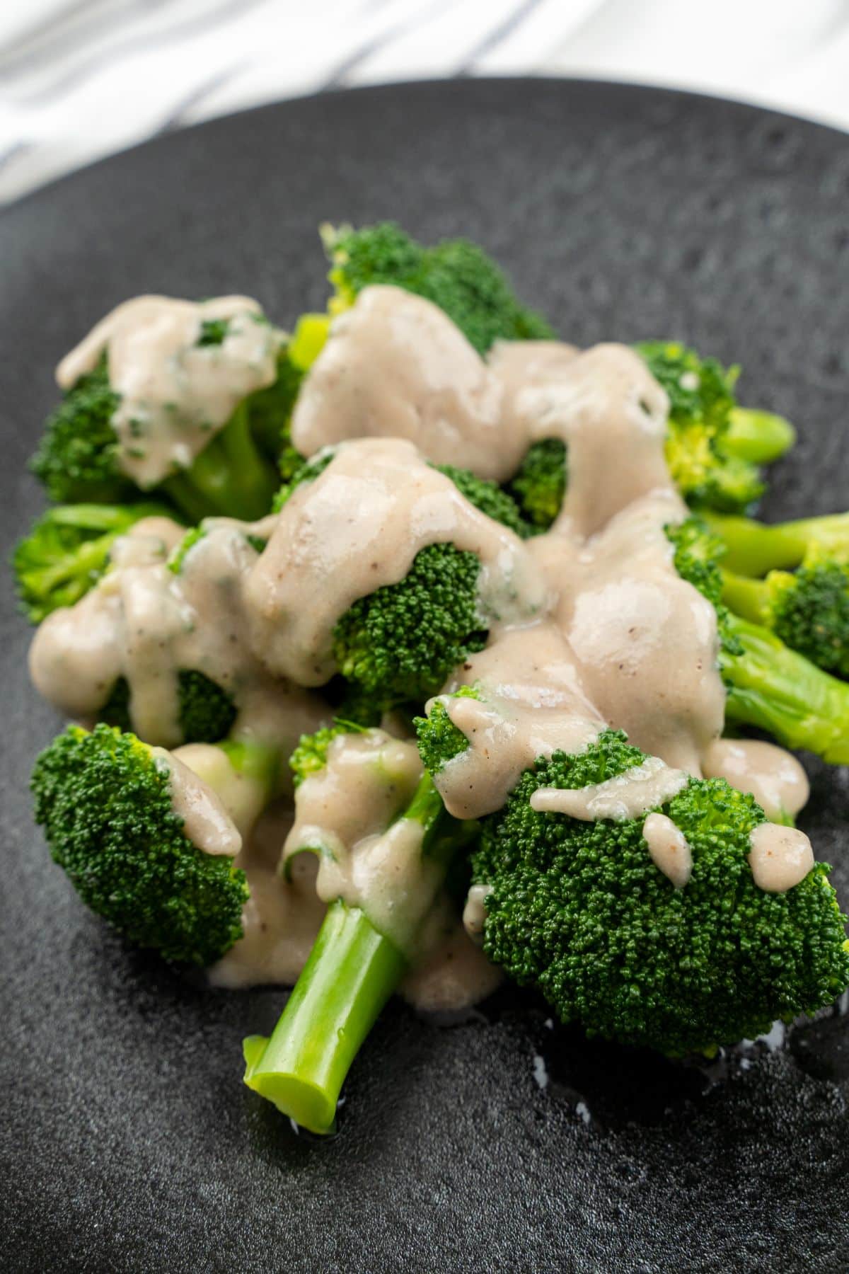 round black plate of broccoli topped with cream sauce