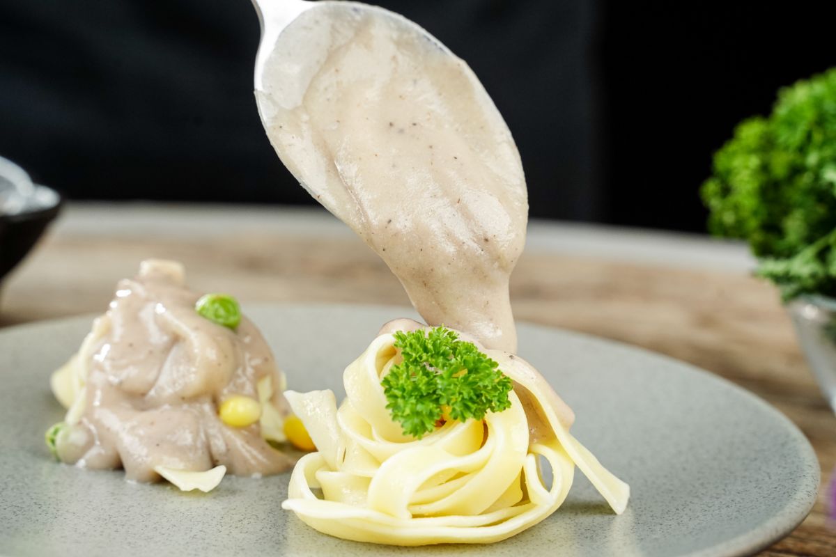 spoon pouring sauce over pasta on gray plate