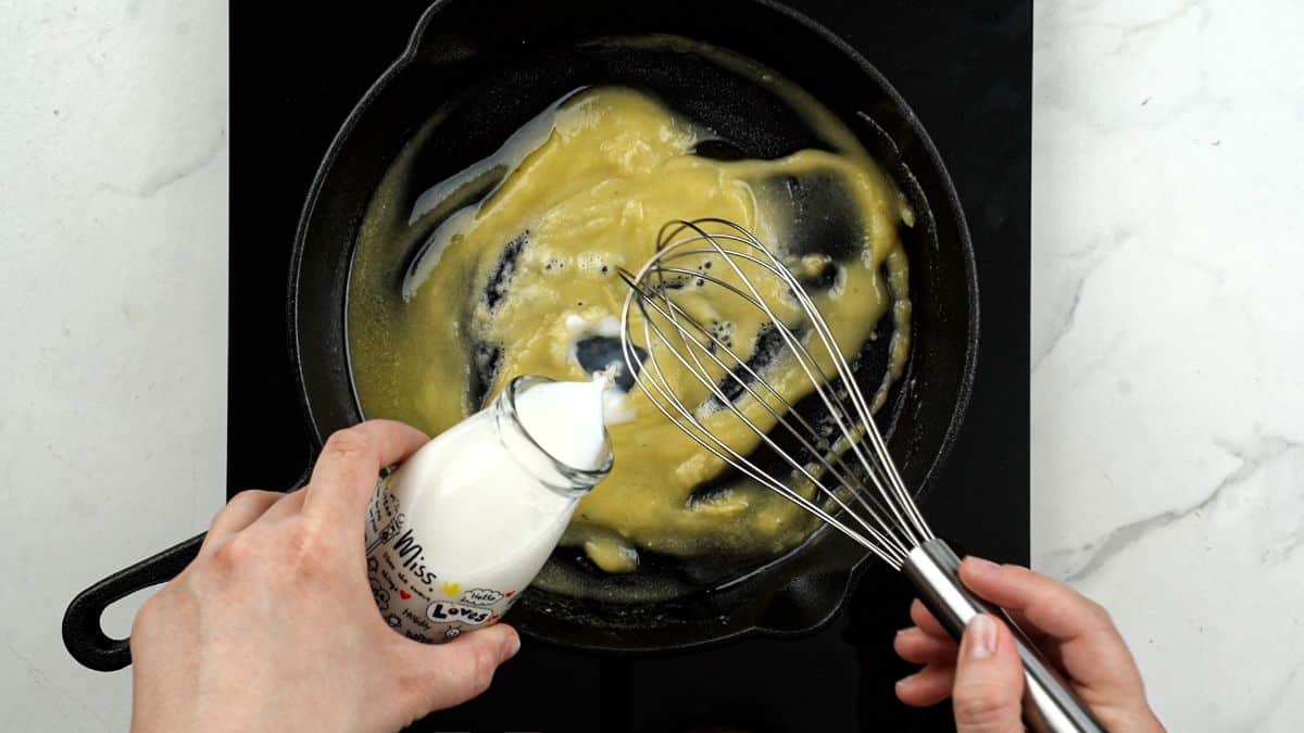 milk being poured into skillet of roux