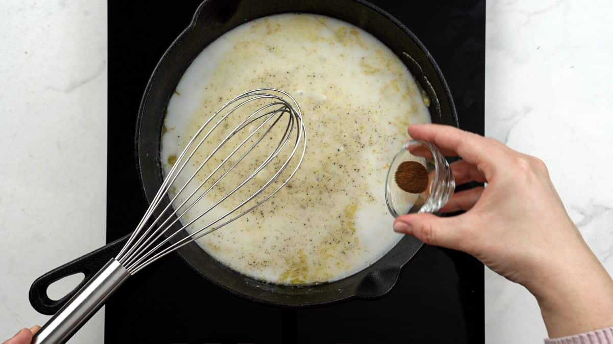 seasonings being added to skillet of sauce with whisk