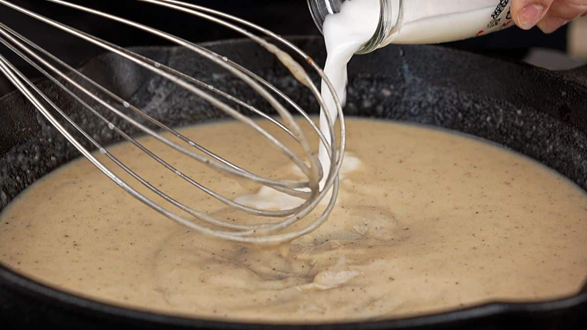 whisking milk into sauce in skillet