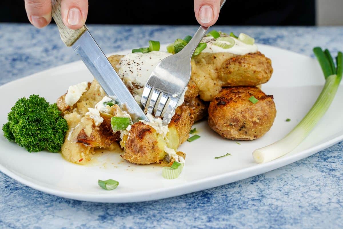 hand holding knife and fork cutting potato on white plate