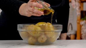 oil being poured over potatoes in glass bowl