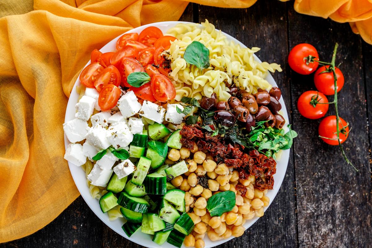 white bowl of vegan Greek pasta salad on wood table with yellow napkin