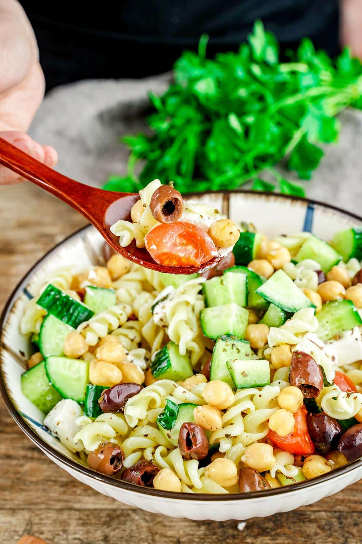 bowl of vegan pasta salad stirred and spoon holding bite above bowl