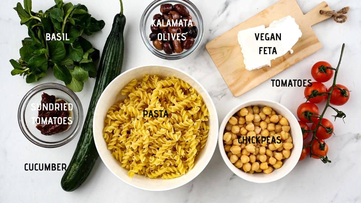 bowls of ingredients on marble table for greek pasta salad