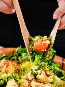 hands holding spoons of mediterranean couscous salad above big bowl