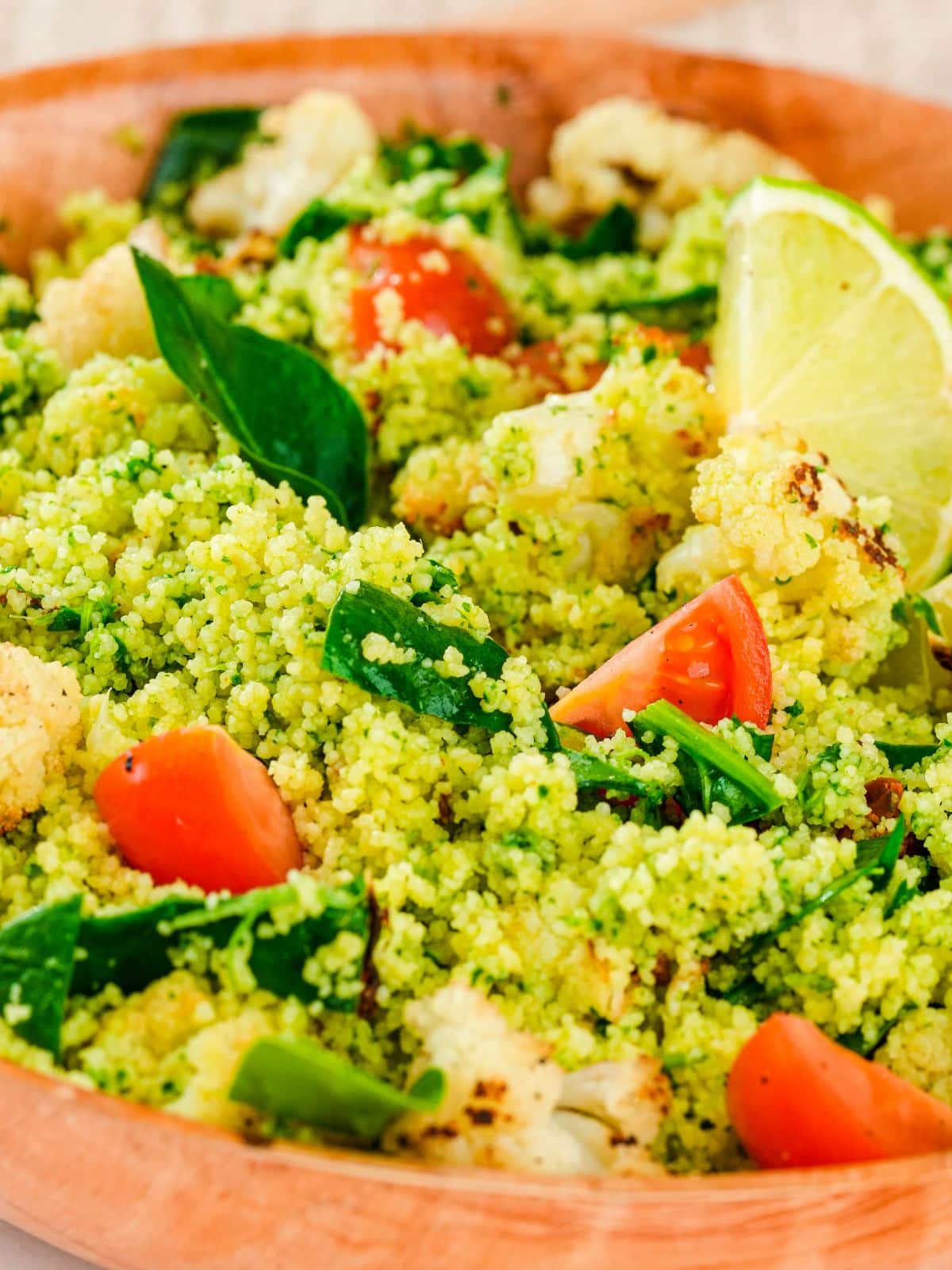 cherry tomato halves and lime wedges on top of wood bowl of couscous salad