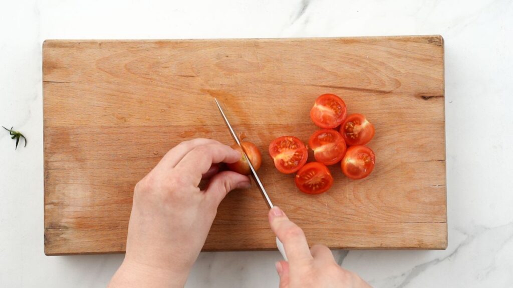 cherry tomatoes being cut on wood cutting board