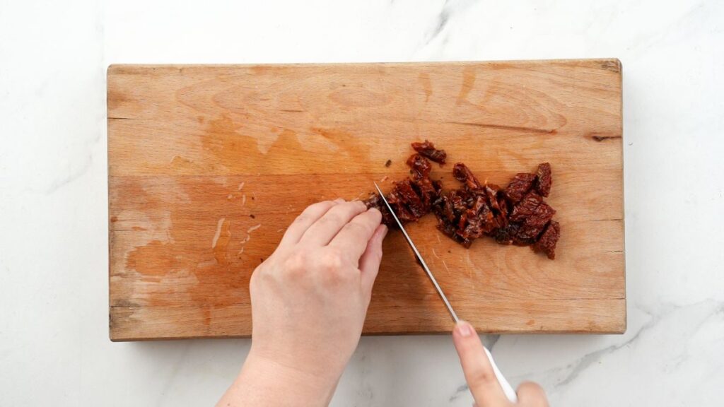 sun dried tomatoes being cut on wood cutting board