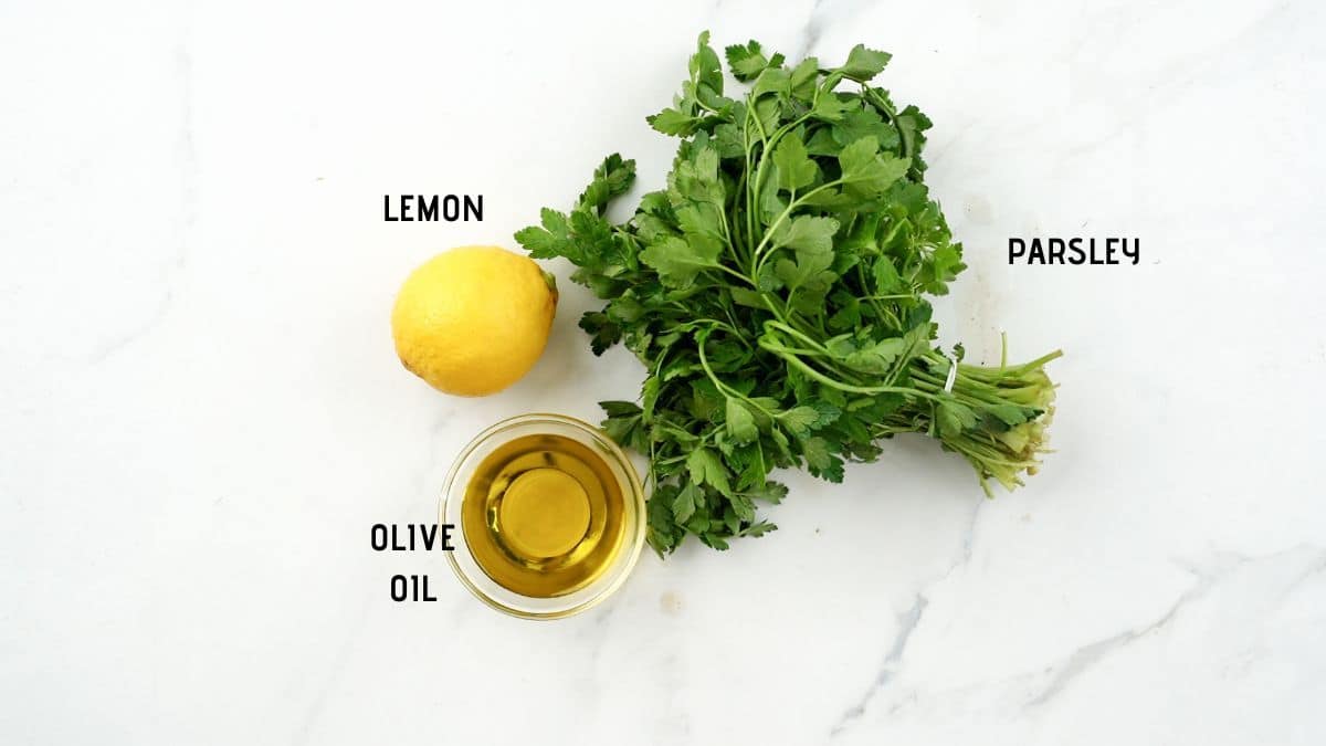 small bowl of oil on marble table next to a lemon and fresh herbs
