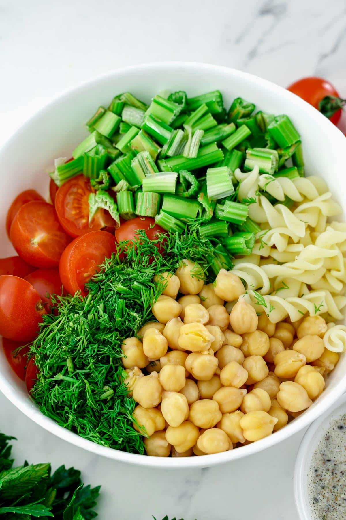 celery, chickpeas, tomato, pasta, and herbs in large white bowl