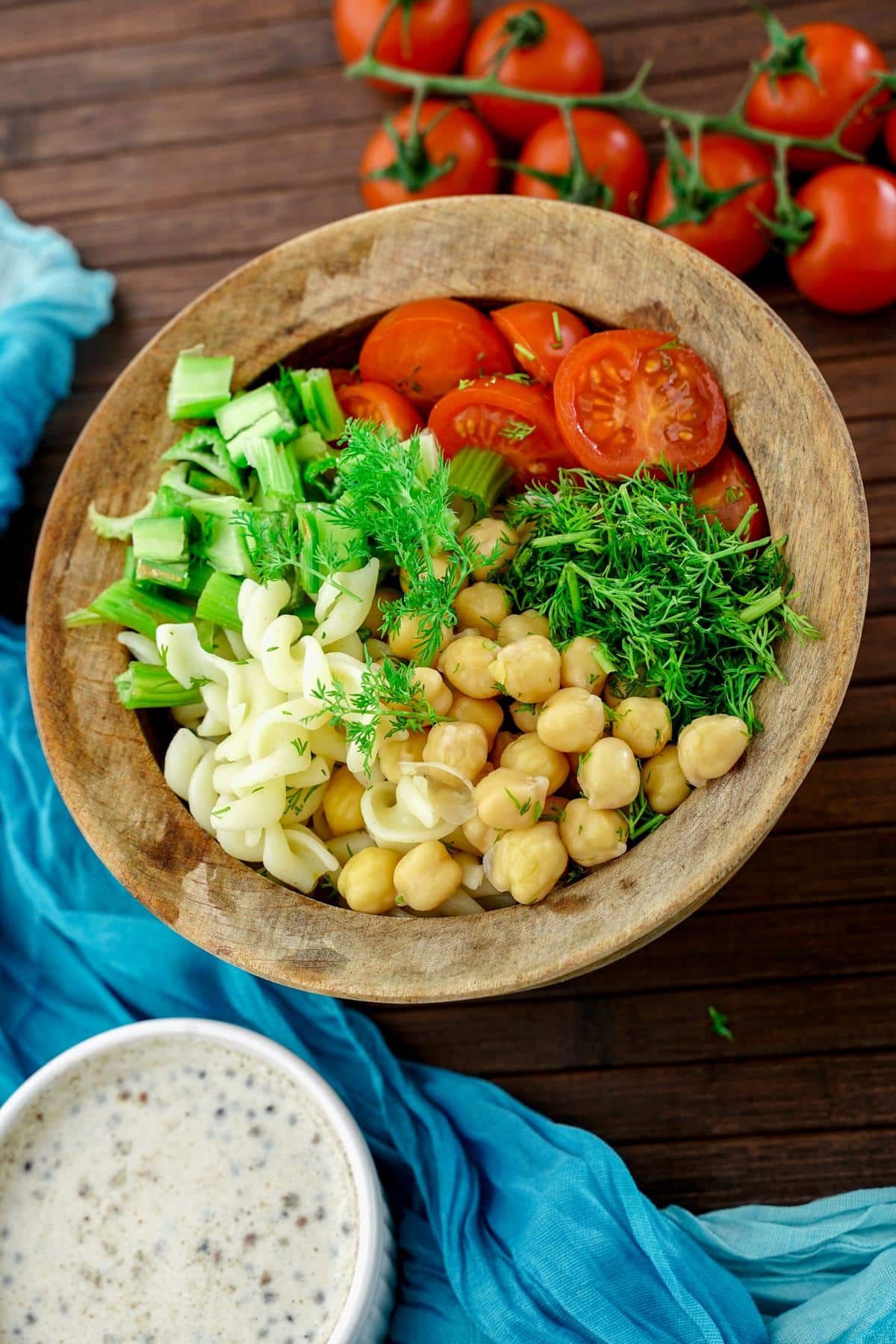 wood bowl filled with chickpeas, pasta, veggies and sauce on table by teal napkin