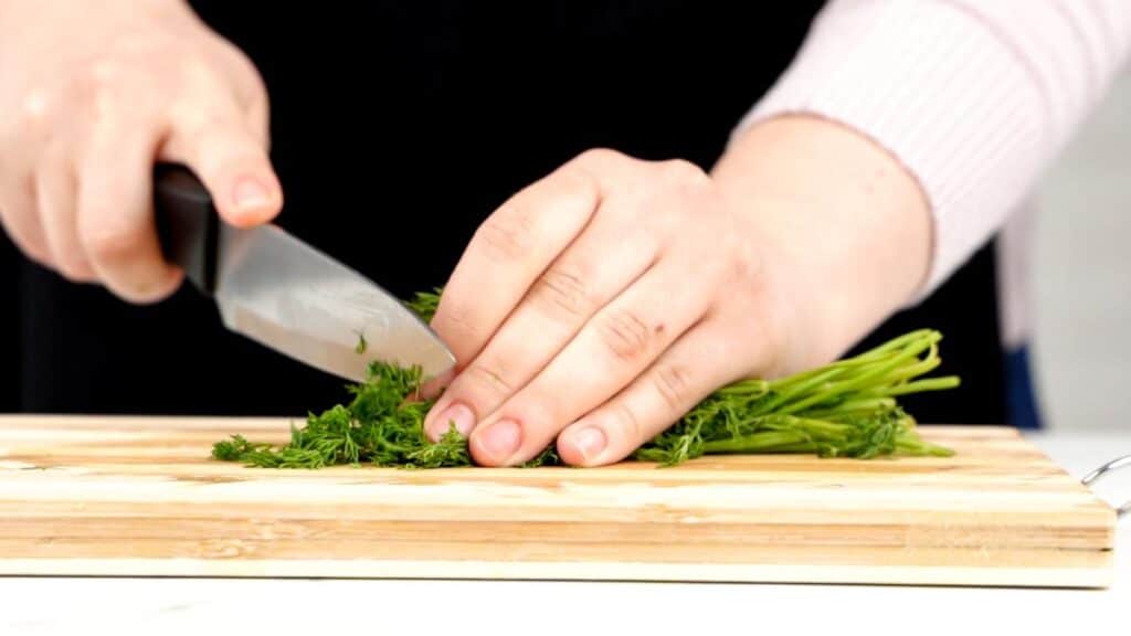 hand chopping fresh herbs on cutting board
